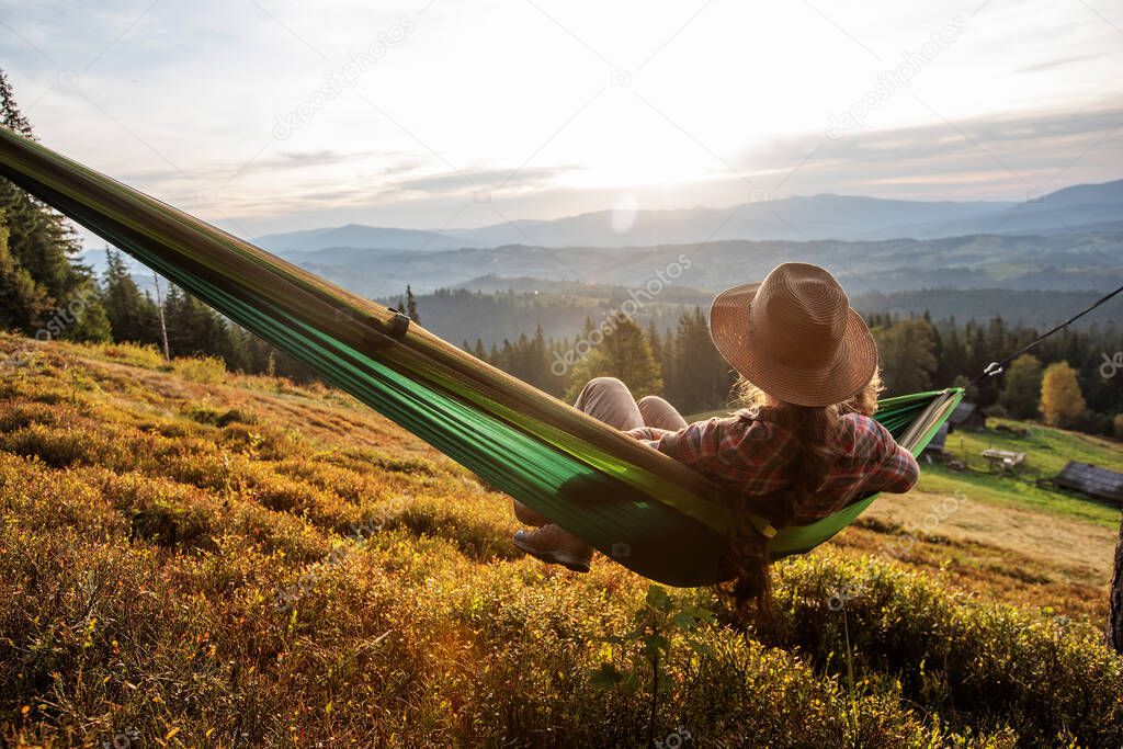 Woman hiker resting after climbing in a hammock at sunset