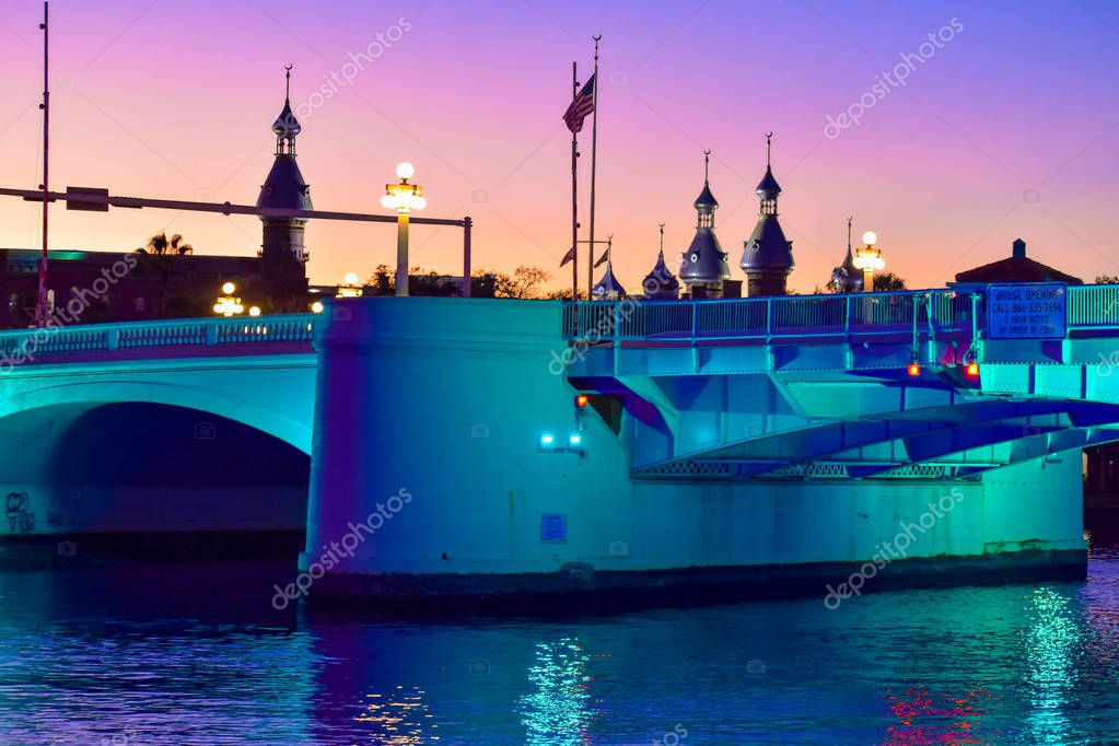 Tampa Bay, Florida. January 05, 2019. Lightblue illuminated bridge in West Kennedy Boulevard and top view of Henry B. Plant Museum on sunset background..