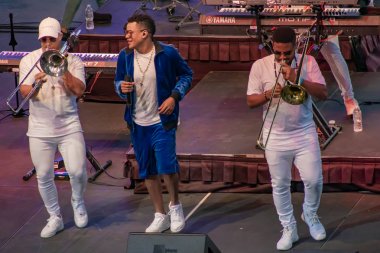 Orlando, Florida. March 17, 2019. Randy Malcom by Gente de Zona dancing with two trumpeters from the band at Seaworld in International Drive Area (2). clipart