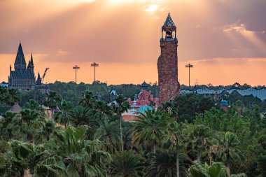 Orlando, Florida. April 18, 2019. Top view of Hogwarts Castle and Island of Adventure lighthouse on colorful sunset sky background at Universal Studios area (3). clipart