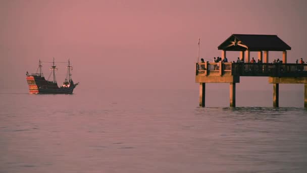 フロリダ州クリアウォータービーチ2019年1月26日 キャプテンメモの海賊クルーズと湾岸ビーチのカラフルな夕日の背景に桟橋で釣り人 — ストック動画
