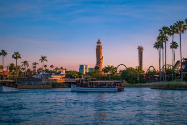 Orlando, Florida. 21 Mayıs 2019. Universal Studios alanında palmiye, uçak, tekne ve Adventure Island deniz feneri ile City Walk iskelesi manzara yaz günbatımı görünümü (2).