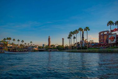 Orlando, Florida. 21 Mayıs 2019. Universal Studios alanında palmiye, uçak, tekne ve Adventure Island deniz feneri ile City Walk iskelesi manzara yaz günbatımı görünümü (1)