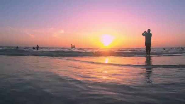 フロリダ州クリアウォータービーチ2019年7月05日水平線上を航行するヨットとピア60エリアで携帯電話で記録する人と美しい夕日 — ストック動画