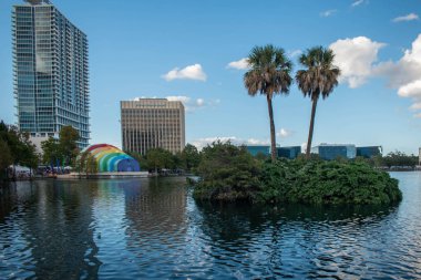 Orlando, Florida. 12 Ekim 2019. Palmiyeli küçük bir ada ve şehir merkezindeki Eola Gölü Parkı 'ndaki Walt Disney Amfitiyatrosunun panoramik manzarası (2)).
