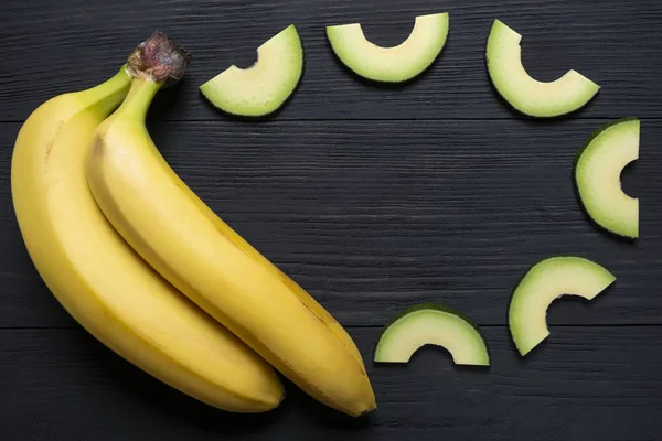 bananas with chopped avocado on a black wooden background