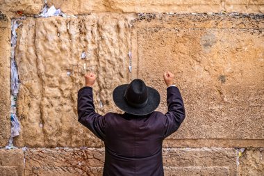 Believing Jew pray near the wall of crying in a big black hat raising his hands uphill clipart