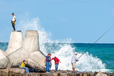 16/11/2018 İskenderiye, Mısır, çocuklar ve yetişkinler ile balıkçılık çubuklar bir beton rıhtım üzerinde beyaz dalgalar iskelede kırma ile balıkçılık olan