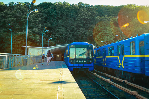 станция открытого типа "Днепр" и поезд метро приближаются к платформе для посадки пассажиров
