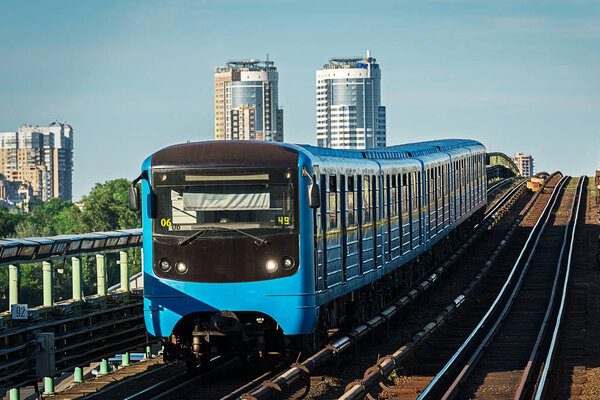 станция открытого типа "Днепр" и поезд метро приближаются к платформе для посадки пассажиров
