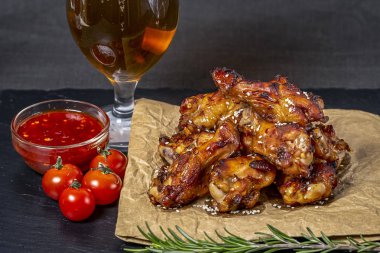 Bir bardak bira ile susam serpilir siyah bir çimento arka plan üzerinde parşömen üzerinde kavrulmuş tavuk kanatları