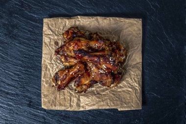 Siyah çimento arka plan üzerinde parşömen üzerinde kavrulmuş tavuk kanatları susam serpilir