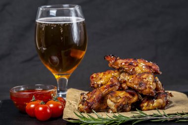 Bir bardak bira ile susam serpilir siyah bir çimento arka plan üzerinde parşömen üzerinde kavrulmuş tavuk kanatları