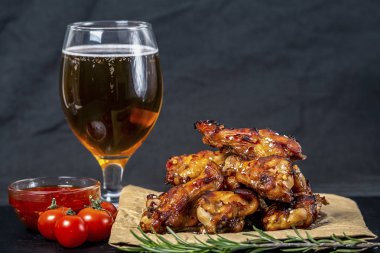 Bir bardak bira ile susam serpilir siyah bir çimento arka plan üzerinde parşömen üzerinde kavrulmuş tavuk kanatları