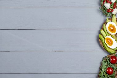 Arugula ile taze avokado sebze ve kopya alanı için bir yer ile gri ahşap arka plan üzerinde mozzarella peyniri ile kızarmış tost üzerinde haşlanmış yumurta ile sandviç Çeşitleri, düz yatıyordu