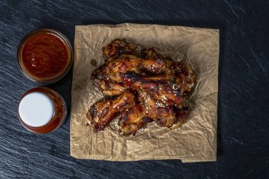 Siyah çimento arka plan üzerinde parşömen üzerinde kavrulmuş tavuk kanatları susam serpilir 