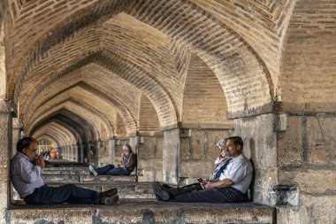 22 / 05 / 2019 İsfahan, İran, insanlar Khaju Köprüsü 'nün altındaki kemerlerde oturup dinleniyorlar, Zayandeh nehri boyunca Khaju Köprüsü' nün gölgesinde üşüyorlar.
