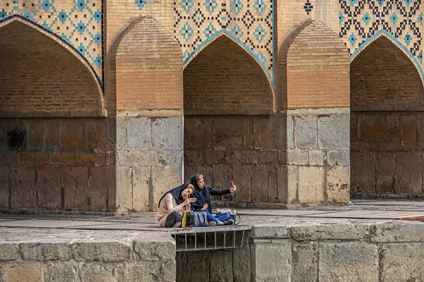 22/05/2019 Isfahan, Iran, two iranian girls is sitting on Khaju Bridge with plenty of arches over Zayandeh river, and make a selfie on smartphone