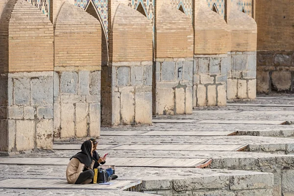 22/05/2019 Isfahan, Iran, two iranian girls is sitting on Khaju Bridge with plenty of arches over Zayandeh river, and make a selfie on smartphone