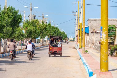 05/11/2019 Hürmüz, Hürmozgan Eyaleti, İran, elleri ile el sallayan neşeli insanlarla dolu caddeden aşağı yaslı bir motosiklet