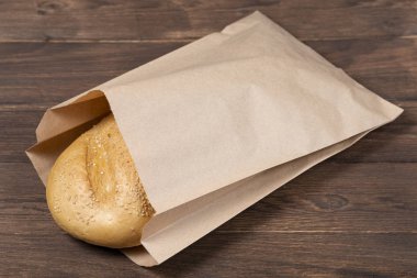 Tahta arka planda geri dönüştürülmüş malzemeden yapılmış bir buhar paketindeki klasik ekmek, kağıt torba konsepti.