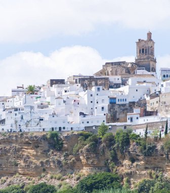 Mavi gökyüzü ve beyaz bulutlar üzerinde kilise, Arcos de la Frontera beyaz evler tarafından çevrili bir hillside içinde 
