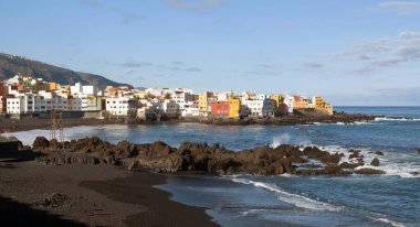 Bir plaj dalgalar içinde İspanyol şehir Puerto de La Cruz ile görüntülemek için bazı kaya denizin ve arka plan otelleri 