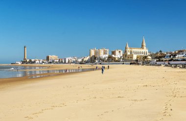Chipiona, Cadiz, Spain-June 2016. Tourists walking along the beach of the turistic municipality of the coast of light in Cadiz on a sunny day. clipart