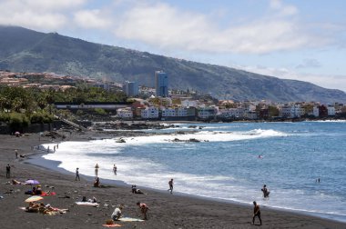 Puerto De La Cruz, Kanarya Adaları, İspanya - Haziran 2016. Anonim turistler bir palmiye ağacı içinde yürüyüş Puerto de la Cruz güneşli bir günde gezi. Onun bir turistik köy deniz kenarında.