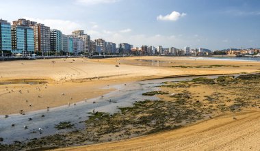 Gijon, İspanya-Eylül 2018. Arka planda şehrin binası ile güneşli bir günde İspanya'nın kuzeyinde Gijon plajında Insanlar.
