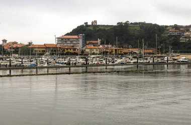 San Vicente de la Barquera, İspanya-Eylül 2018. Sahilde tekne ve bulutlu bir günde sokakta yürüyen insanlar ile denize yakın İspanyol şehir.