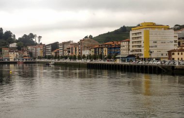 San Vicente de la Barquera, İspanya-Eylül 2018. Sahilde tekne ve bulutlu bir günde sokakta yürüyen insanlar ile denize yakın İspanyol şehir.