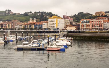 San Vicente de la Barquera, İspanya-Eylül 2018. Sahilde tekne ve bulutlu bir günde sokakta yürüyen insanlar ile denize yakın İspanyol şehir.