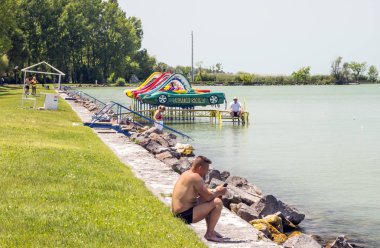 Balatonlelle, Macaristan-Haziran 2019. Güneşli bir günde şehrin gölü yakınında bir yaz günü çim turist.