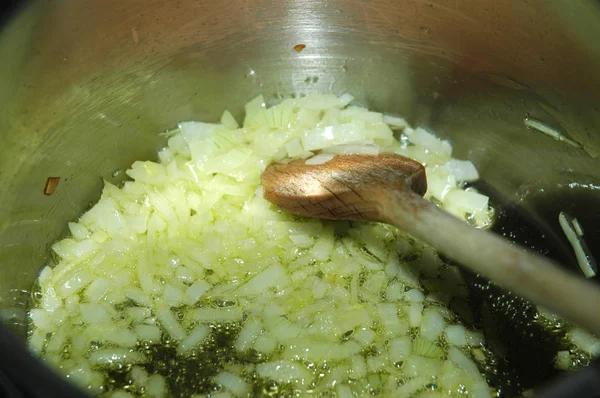 cut white onions frying in oil in stainless steel cooking pot with wooden spoon