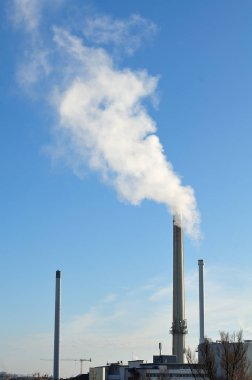 bir şehirde sanayi bölgesi üzerinde beyaz duman yayan Bacalı görüntülemek