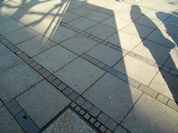shadows of person, building and tree on pavement of a pedestrian zone