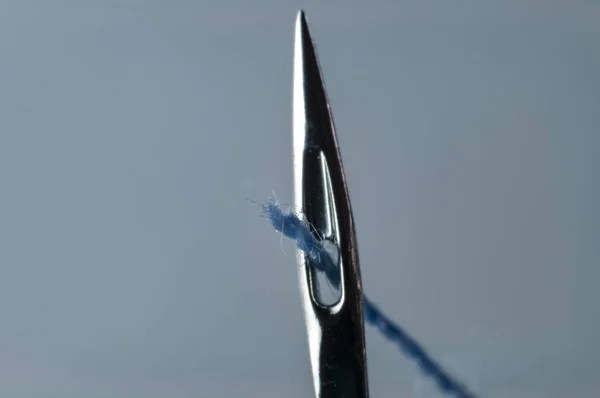 eye of a sewing machine needle with blue thread led through it