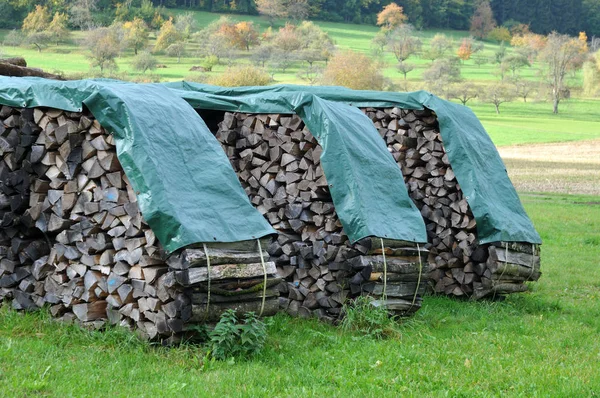 Stacks of firewood drying on meadow covered with plastic tarps — 스톡 사진