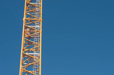 Mavi gökyüzü olan bir şehirde, turuncu boyalı kafesli bir vinç.