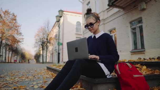 Szép csípő tini lány ül a járdán őszi város utca és működő laptop számítógép. Iskolás szabadtéri jegyzettömbödbe. Szép őszi Időjárás. — Stock videók