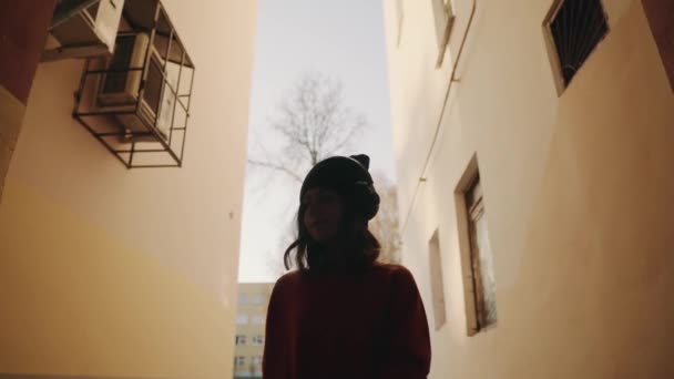 Söt ung flicka gågatan mellan byggnader och lyssnar musik i hörlurar, urban stil, snygg hipster tonåring i svart hatt lyssna musik och leende, orange galna stil — Stockvideo