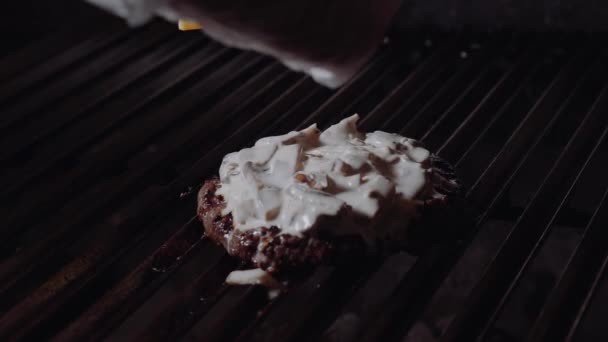 Chef préparant un hamburger. L'homme met du fromage sur les hamburgers et le fait fondre sur la cuisinière . — Video