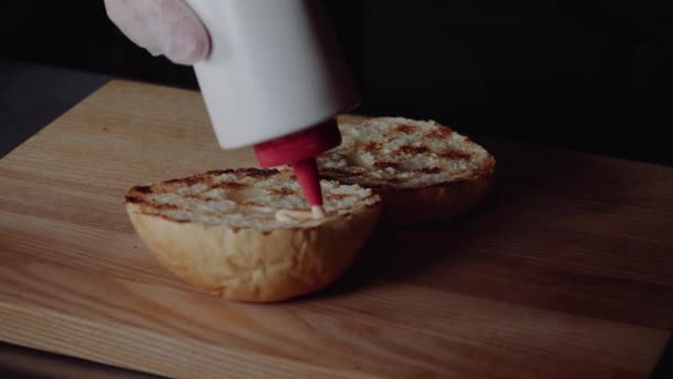 Chef preparando la hamburguesa. De cerca - mano del hombre unta salsa frito hamburguesa para una hamburguesa . — Vídeo de stock