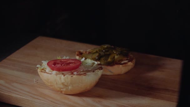 Шеф-повар готовит бургер, жарит булочку на гриле, нарезает помидоры — стоковое видео