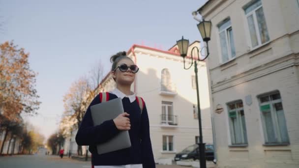 Bella ragazza hipster teen a piedi lungo la vecchia strada della città e sorridente. Studentessa con borsa rossa che tiene in mano il portatile. Bel tempo autunnale . — Video Stock