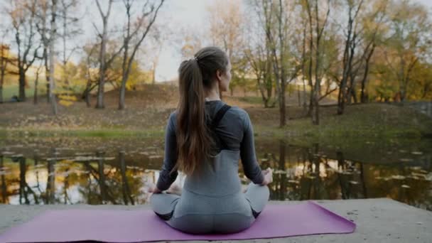 Молодая женщина практикует йогу на открытом воздухе. Женщина медитирует на открытом воздухе перед красивой осенней природой . — стоковое видео