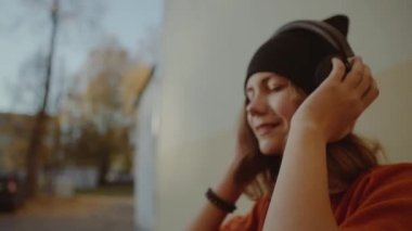 Sevimli Genç kız kulaklık ve dans, kentsel tarzı, şık hipster teen siyah şapka dinle müzik ve gülümseme sarı duvarına, turuncu çılgın sokak stil infront müzik dinleme