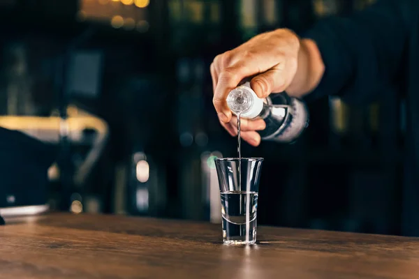 Mano di barman con bottiglia che versa la bevanda in vetro. Barista versando forte bevanda alcolica in piccolo bicchiere sul bar, colpi, su sfondo luminoso . — Foto Stock