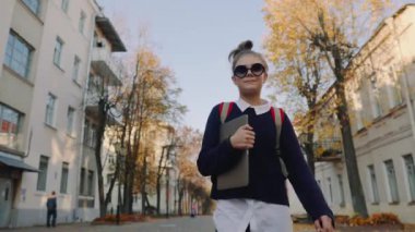 Eski Şehir caddeden aşağı yürüyüş ve gülümseyen güzel hipster genç kız. Kırmızı çanta laptop elinde tutan ile kız öğrenci. Güzel sonbahar hava.